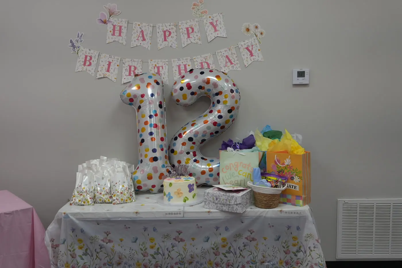 A birthday banner and balloons above a decorated gift table.