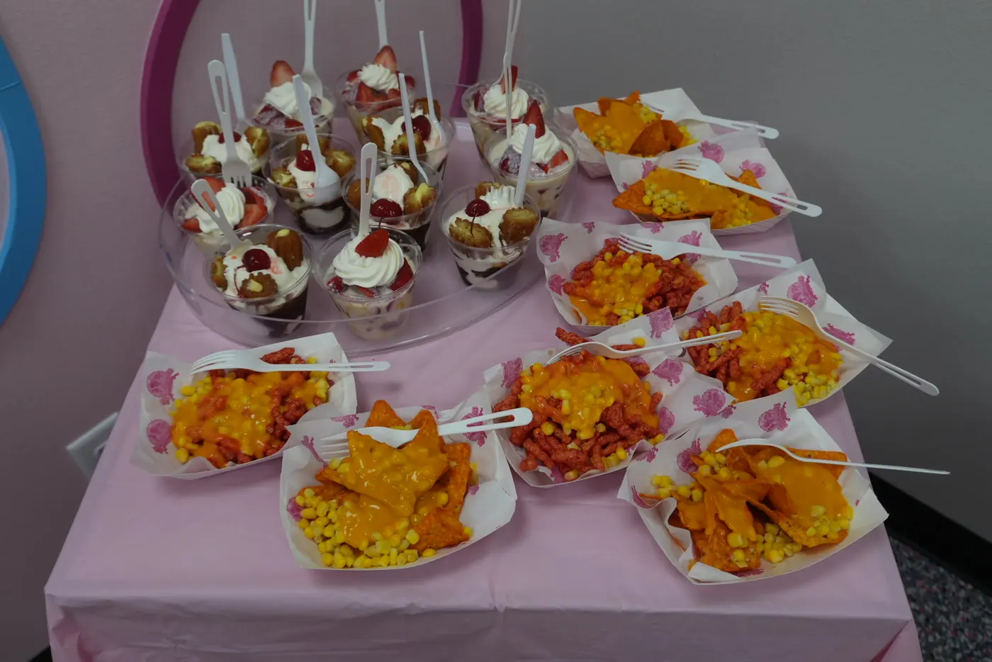 Dessert cups and snack plates arranged on a pink tablecloth.