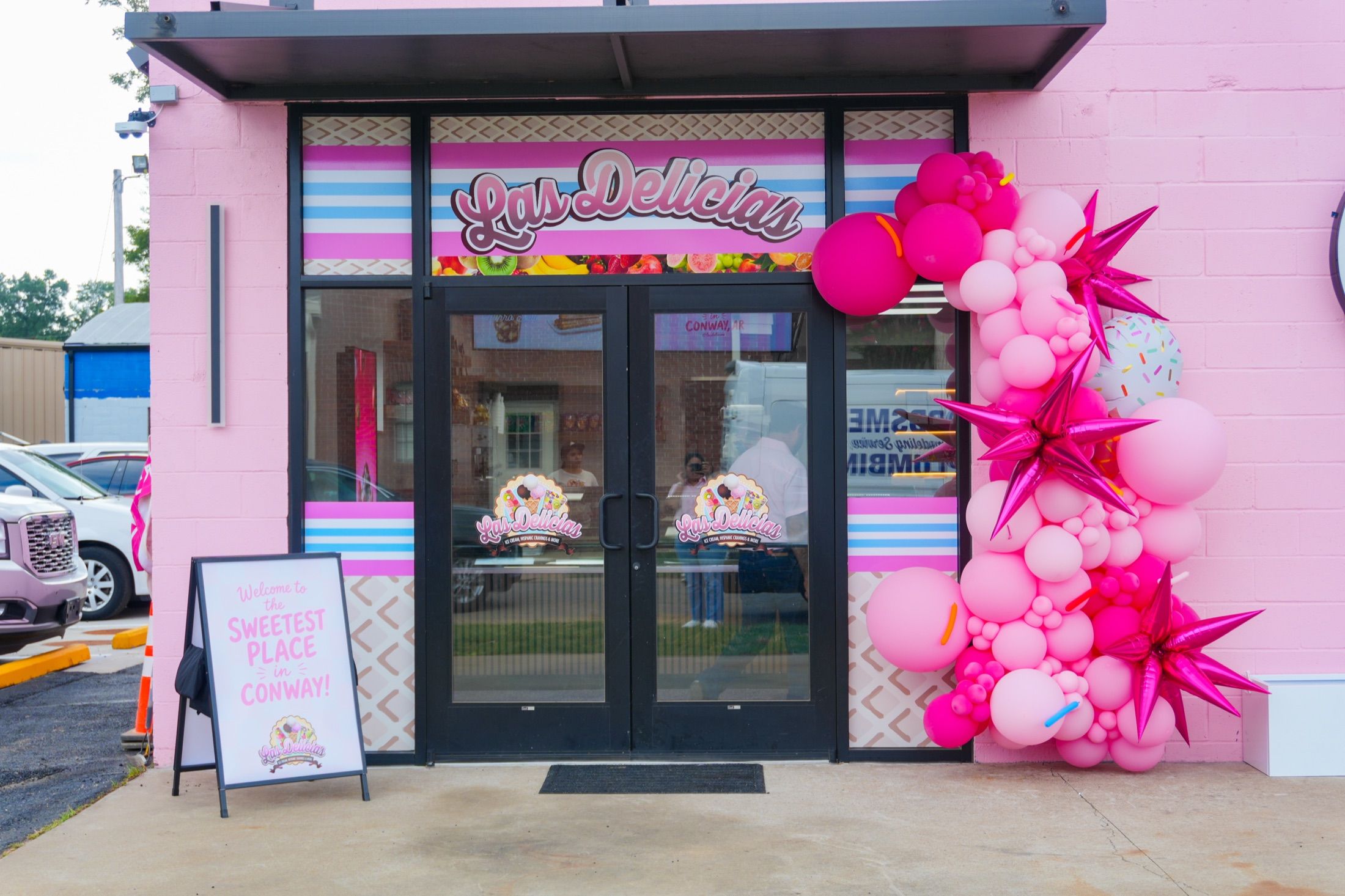 The pink Harkrider Street entrance on opening day, with a balloon arch and a sign reading welcome to the sweetest place in Conway